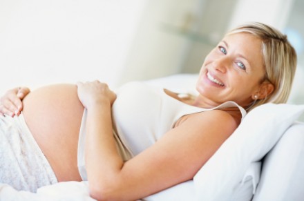 Mosolygó kismama pihen egy fehér kanapén
